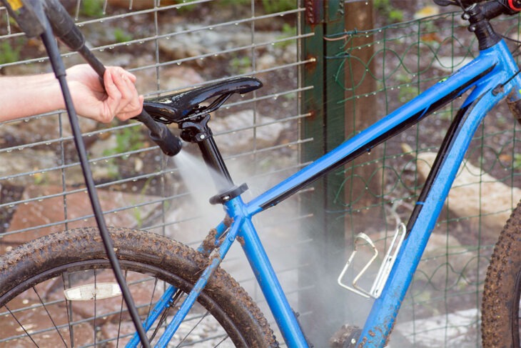 Ein blaues Fahrrad mit einem Hochdruckreiniger absprühen.